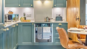 A kitchen with teal cabinets, a wooden door, a stove, a sink, and a dining area with a chair and table. - 3 Bed in King's Lynn (oc-96035) (Middleton)