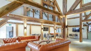 A spacious interior with high ceilings and exposed wooden beams, featuring leather sofas and a dining area. - 3 Bed in King's Lynn (oc-96036) (Middleton)