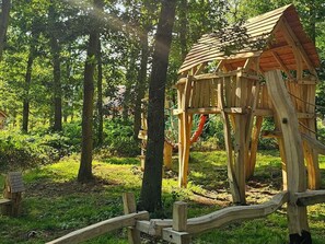 A wooden playhouse in a forested area with a rope swing. - 3 Bed in King's Lynn (oc-96036) (Middleton)