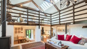 A spacious loft-style living area with a high ceiling, exposed wooden beams, a fireplace, a sofa with red cushions, and a dining area with a table and chairs. - 1 Bed in Tavistock (oc-96009) (Cudlipptown)