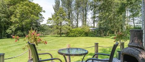 A deck with wicker chairs and a glass table, surrounded by a grassy lawn and trees.