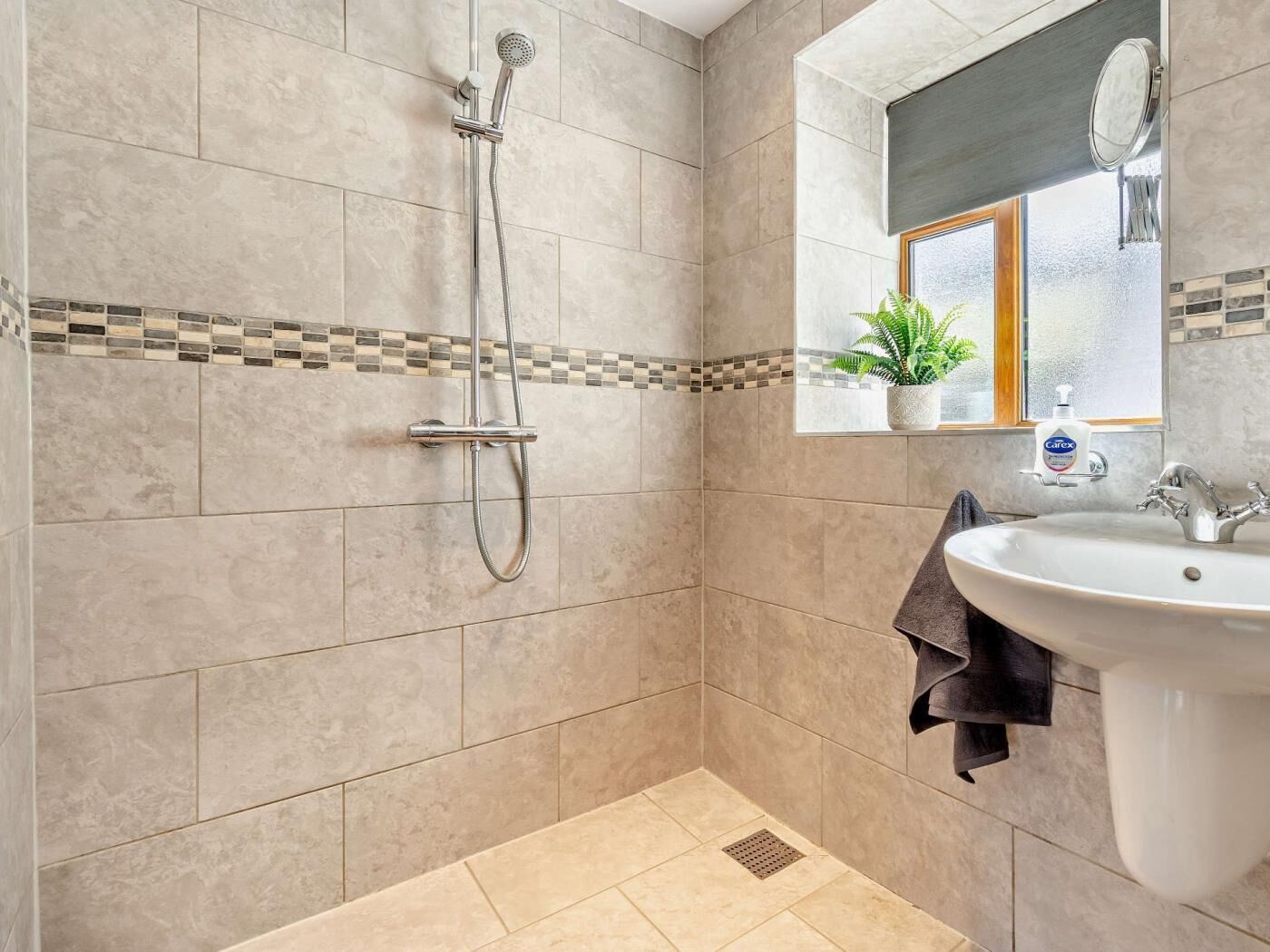 A bathroom with a shower, sink, and a window with a plant.