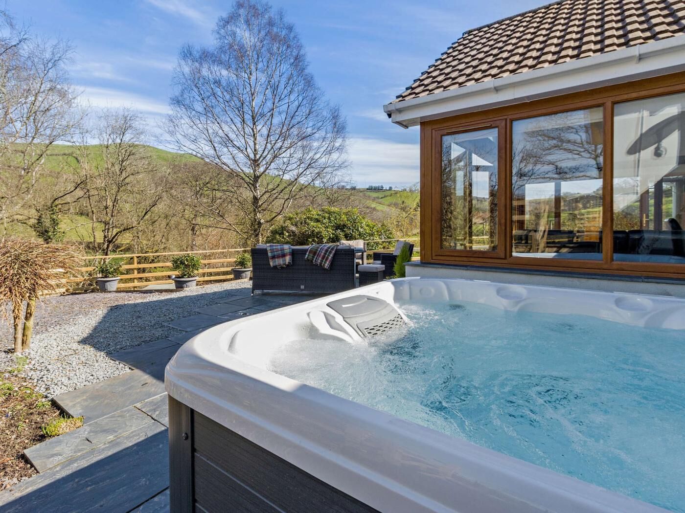 Een hottub met een houten terras, een zithoek met een tafel en stoelen, en uitzicht op het omliggende landschap.