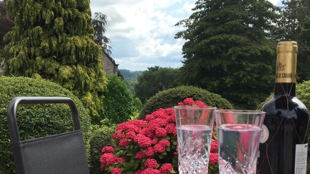 A table with a bottle of wine and two glasses, set outdoors with a view of a garden and trees. - 2 Bed in Matlock (oc-75893) (Slaley)