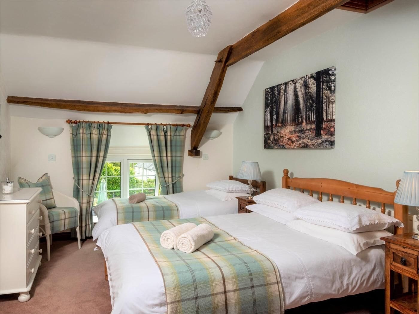 A bedroom with two beds, a dresser, a painting of a forest, and a window with curtains.
