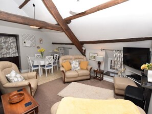 A cozy living room with a sofa, armchair, and a television. There is a dining table with chairs and a lamp. - 2 Bed in Brecon (oc-bn178) (Llanfihangel Nant Bran)