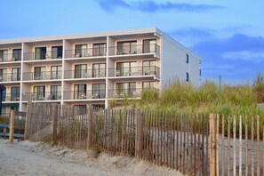 Ein mehrstöckiges Hotel mit Balkonen in der Nähe eines Sandstrandes mit Holzzaun.