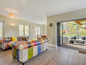 A modern living room with a large sectional sofa, a dining area with outdoor seating, and a large sliding glass door leading to a garden. - 2 Bed in King's Lynn (oc-96048) (Middleton)