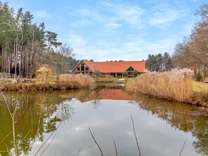 A lakeside building with a red roof, surrounded by tall trees and reeds. - 2 Bed in King's Lynn (oc-96048) (Middleton)