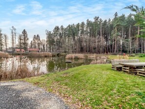 Blick auf einen See mit einem Steg, einer Rasenfläche und einem Wald im Hintergrund.