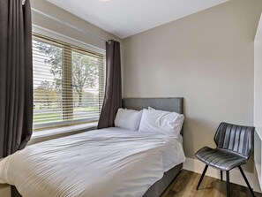 Ein Schlafzimmer mit einem Bett, einem Sessel und einem Fenster mit Vorhängen.