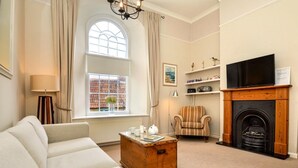 A living room with a sofa, a wooden coffee table, a fireplace, a television, and a window with curtains. - 2 Bed in Beaminster (oc-78567) (Beaminster)