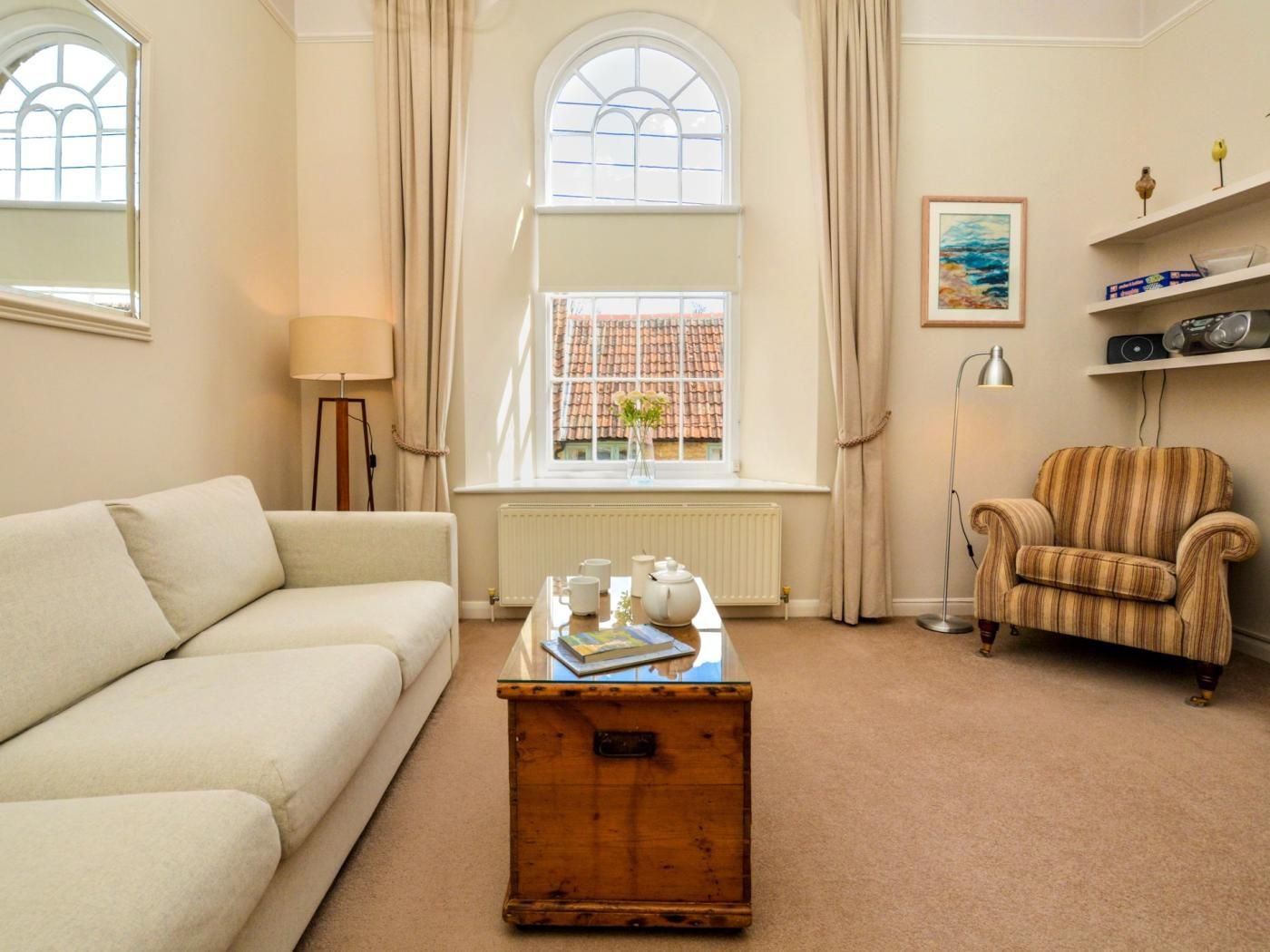 A living room with a sofa, armchair, wooden coffee table, and a window with curtains.