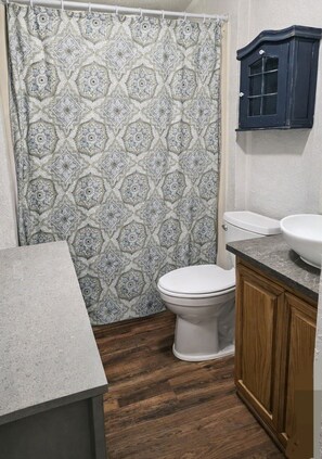 A bathroom with a patterned shower curtain, a white toilet, a wooden cabinet, and a granite countertop. - 4 bed, 2 bath house in Kingston, OK between Catfish Bay & Alberta Creek Marinas. (Kingston)