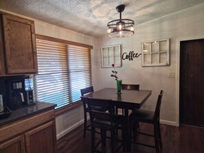 A dining area with a table, chairs, a coffee sign, and a window with blinds. - 4 bed, 2 bath house in Kingston, OK between Catfish Bay & Alberta Creek Marinas. (Kingston)
