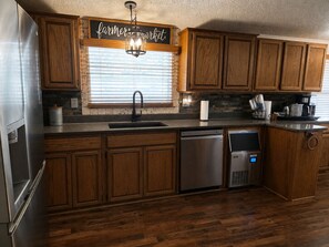 A kitchen with wooden cabinets, a stainless steel refrigerator, a dishwasher, and a farmhouse-style window with blinds. - 4 bed, 2 bath house in Kingston, OK between Catfish Bay & Alberta Creek Marinas. (Kingston)