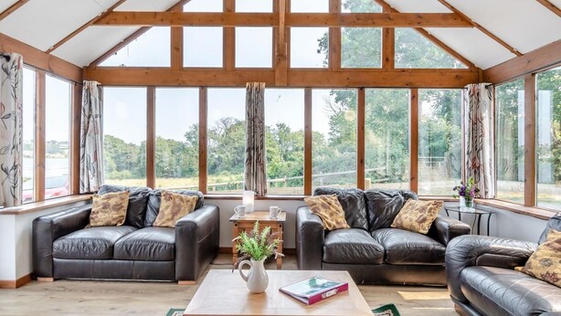 A spacious room with a high ceiling and large windows, featuring two leather sofas and a wooden coffee table. - 3 Bed in Pembroke (oc-44349) (Hundleton)