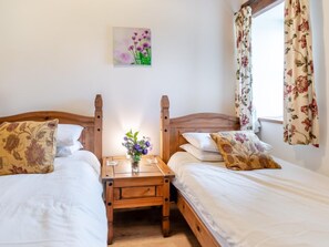 A twin room with two beds, a wooden nightstand, a vase with flowers, and a painting on the wall. - 3 Bed in Pembroke (oc-44349) (Hundleton)