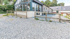 A modern building with large windows, a gravel driveway, and a wooden fence. - 3 Bed in Pembroke (oc-44349) (Hundleton)