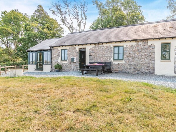 A stone building with a gravel driveway and a wooden fence. - 3 Bed in Pembroke (oc-44349) (Hundleton)