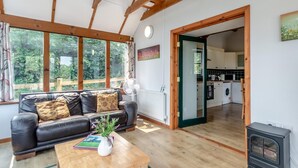 A living room with a sofa, a coffee table with a plant, and a view through large windows to the outdoors. - 3 Bed in Pembroke (oc-44349) (Hundleton)