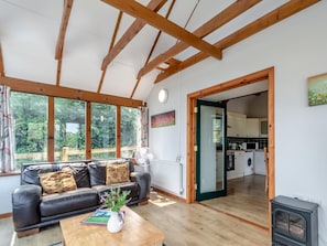 Ein Wohnzimmer mit einer Couch, einem Couchtisch mit Pflanze und Blick durch große Fenster ins Freie.
