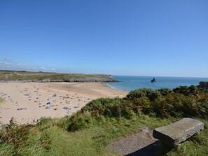 A beach with people, tents, and a rocky outcrop in the distance. - 3 Bed in Pembroke (oc-44350) (Hundleton)