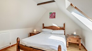 Een slaapkamer met een schuine kap, een houten bed, twee nachtkastjes met lampen en een enkel wanddecoratie.