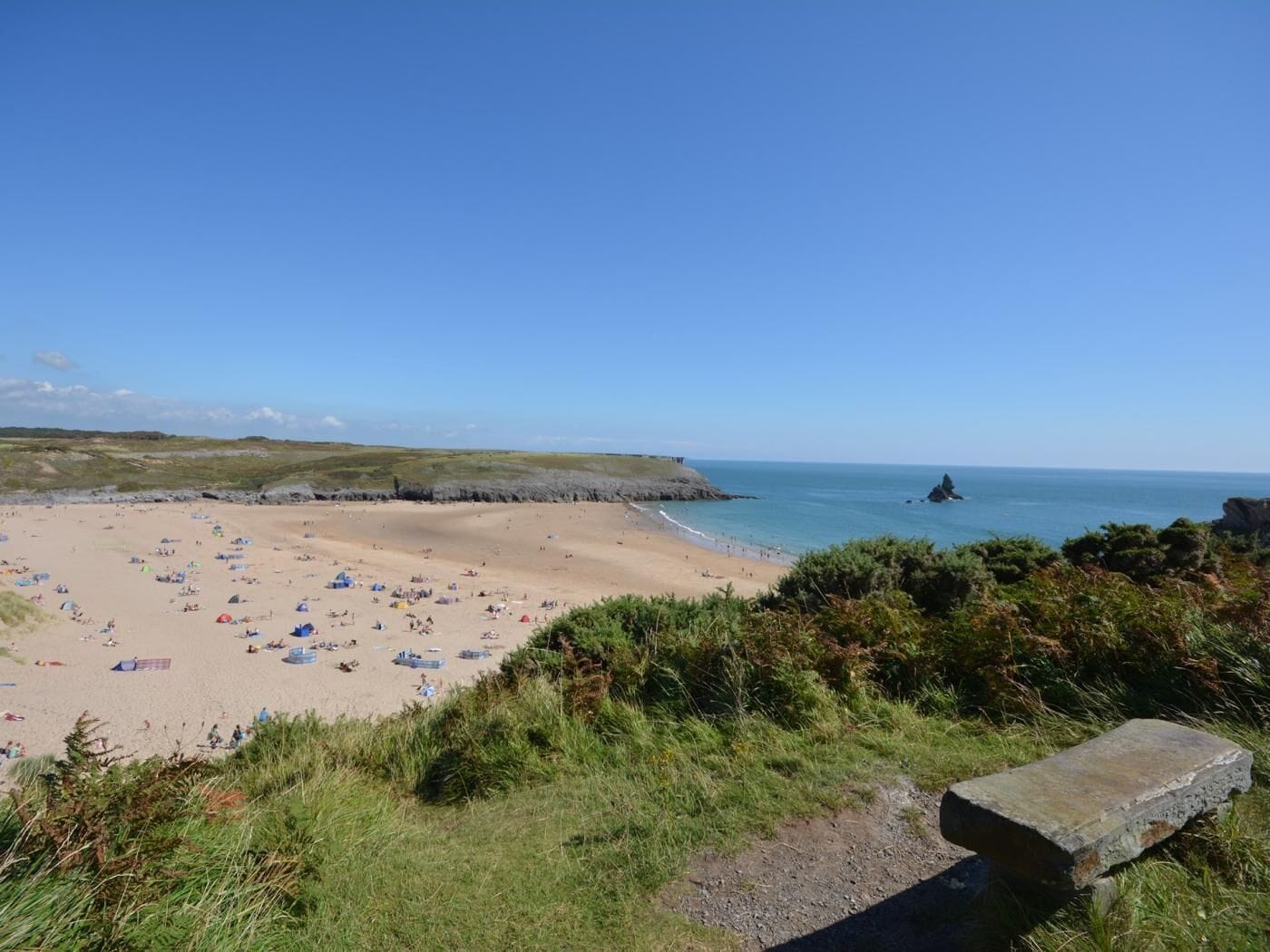 A beach with tents and people, a rocky outcrop, and a clear sky.
