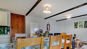 Un coin repas avec des chaises en bois, une table recouverte d’une nappe à motifs floraux et un luminaire suspendu.