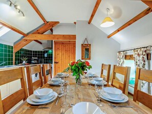Comedor con una mesa de madera dispuesta para cuatro, techo de madera y vista a una cocina.