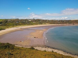 A coastal beach with a sandy shore, a few vehicles, and a clear sky. - 4 Bed in Pembroke (oc-44351) (Hundleton)