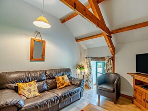 A living room with a leather sofa, a wooden chair, a television, and a wooden cabinet. - 4 Bed in Pembroke (oc-44351) (Hundleton)