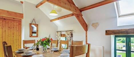 Un coin repas avec une table en bois dressée pour quatre personnes, un miroir et une fenêtre donnant sur un paysage verdoyant.