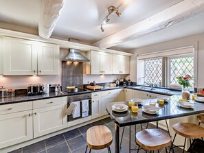 A modern kitchen with white cabinets, a central island with stools, a built-in oven, and a large window with a view. - 5 Bed in Halifax (oc-96061) (Sowerby Bridge)