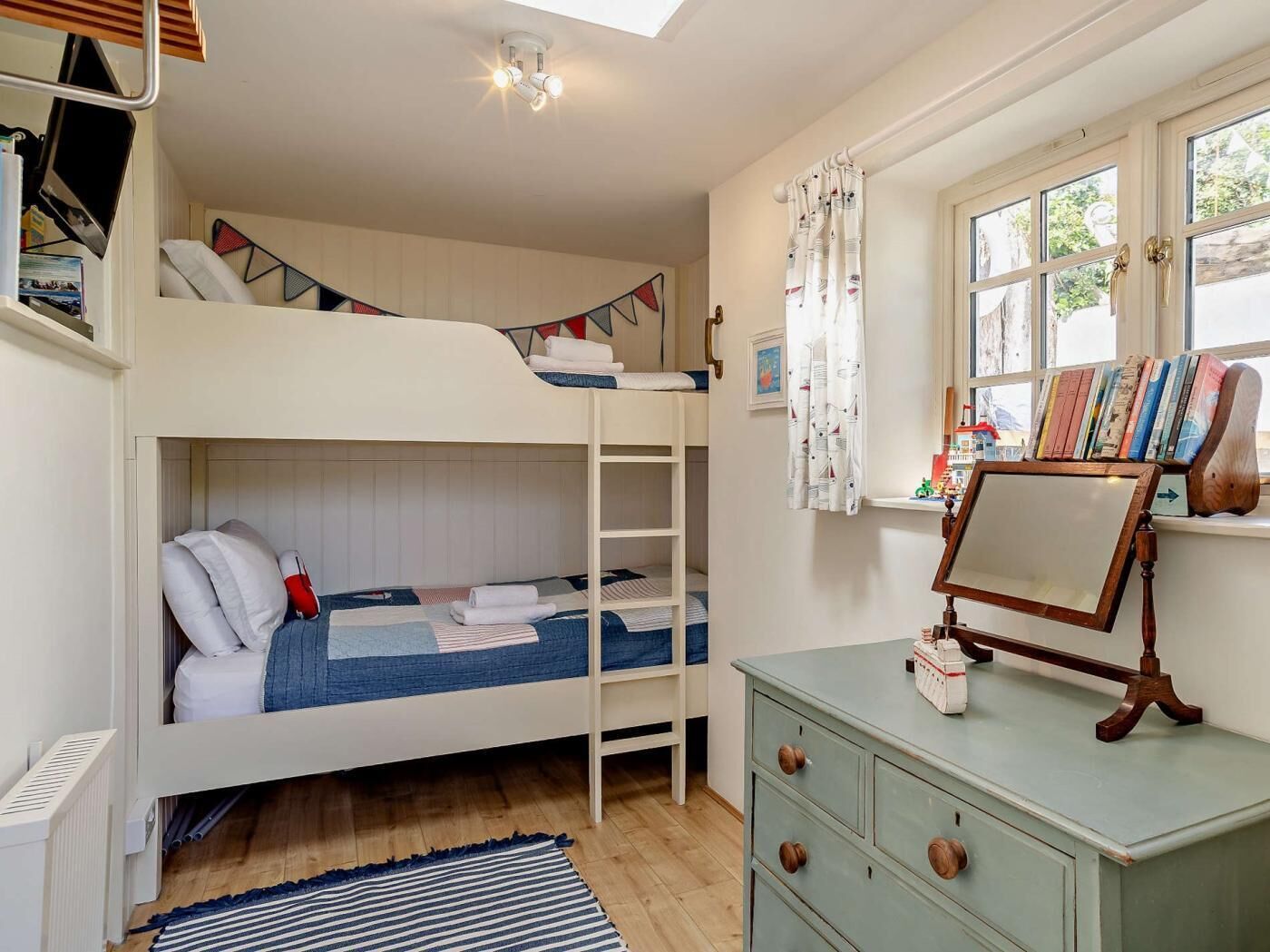 Een slaapkamer met een stapelbed, bureau, boeken en een raam.