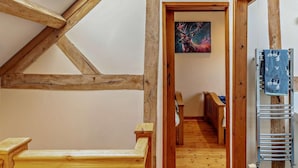 Een kamer met een schuine plafond, houten balken, een bankje, een schilderij en een handdoekhouder.