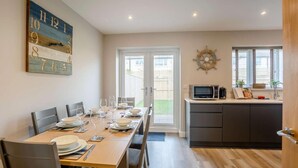 A dining area with a table set for four, a kitchen with a microwave, and a door leading outside. - 3 Bed in Seahouses (oc-81486) (Seahouses)