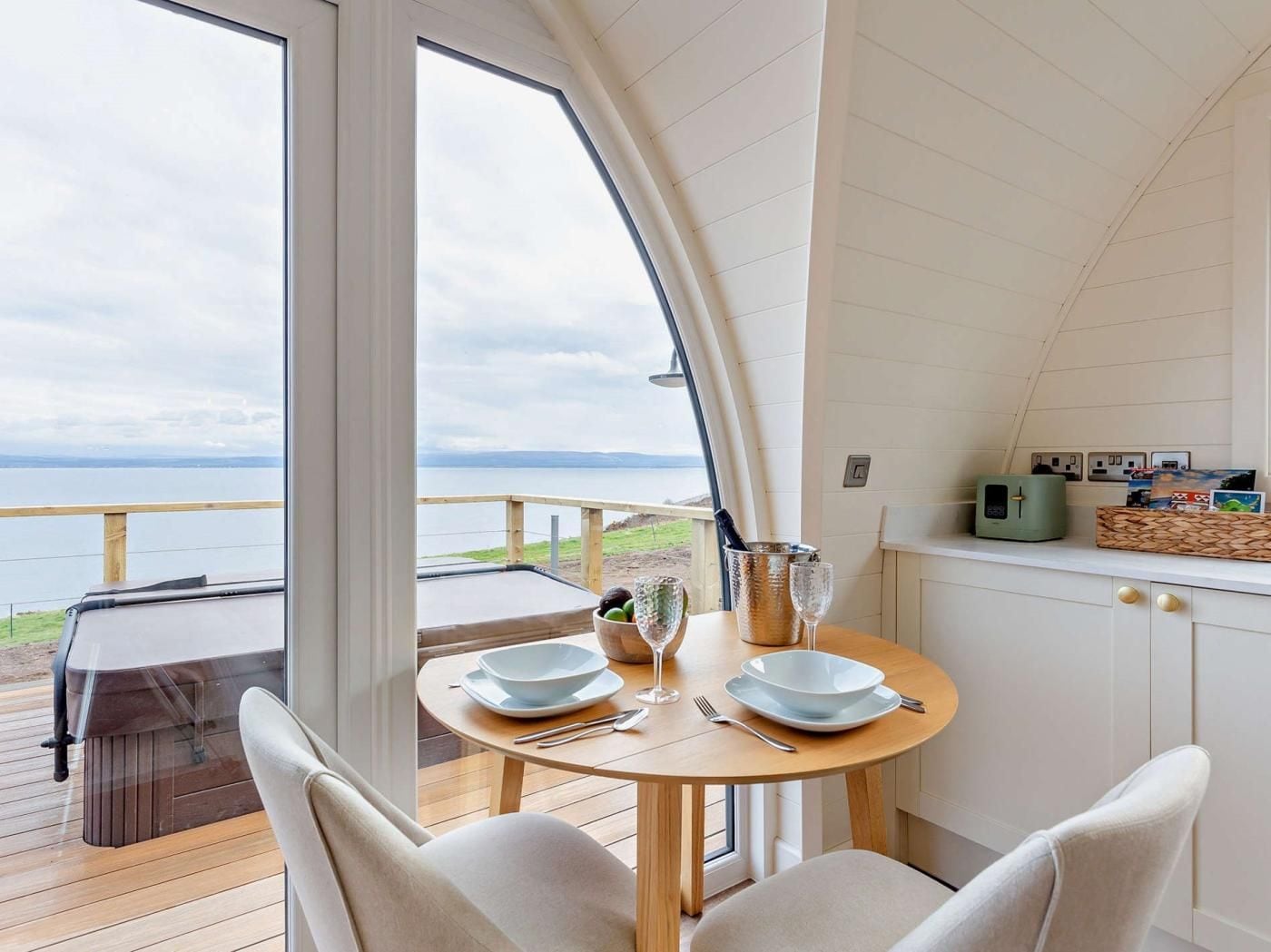 A dining area with a view of the sea, a table set with plates and cutlery, and a bottle of champagne.