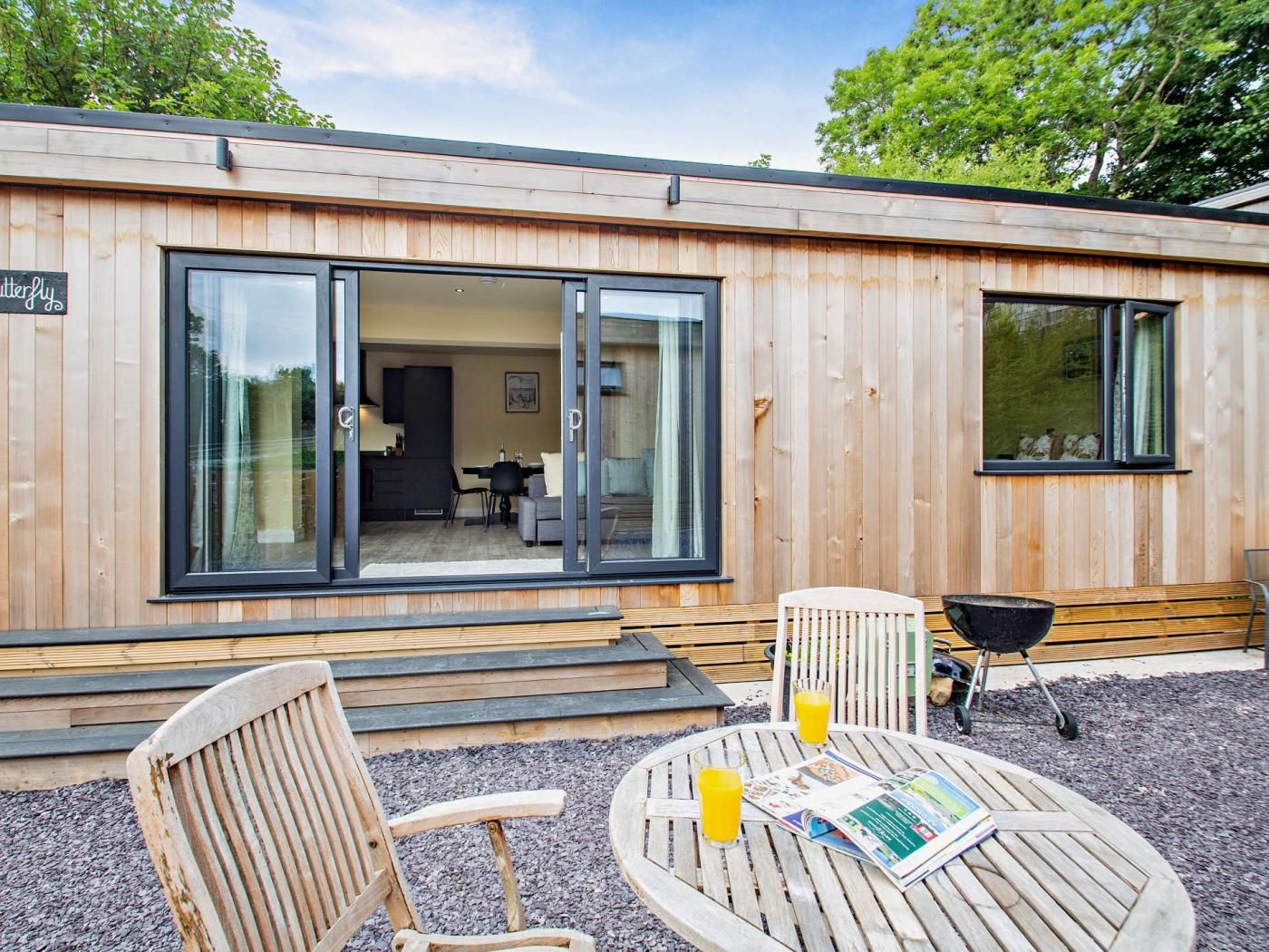 Une cabane en bois avec une porte-fenêtre coulissante, un petit patio avec une table ronde, deux chaises et un barbecue.