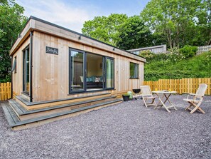 En træhytte med stor skydedør, terrasse og udendørs møbler.