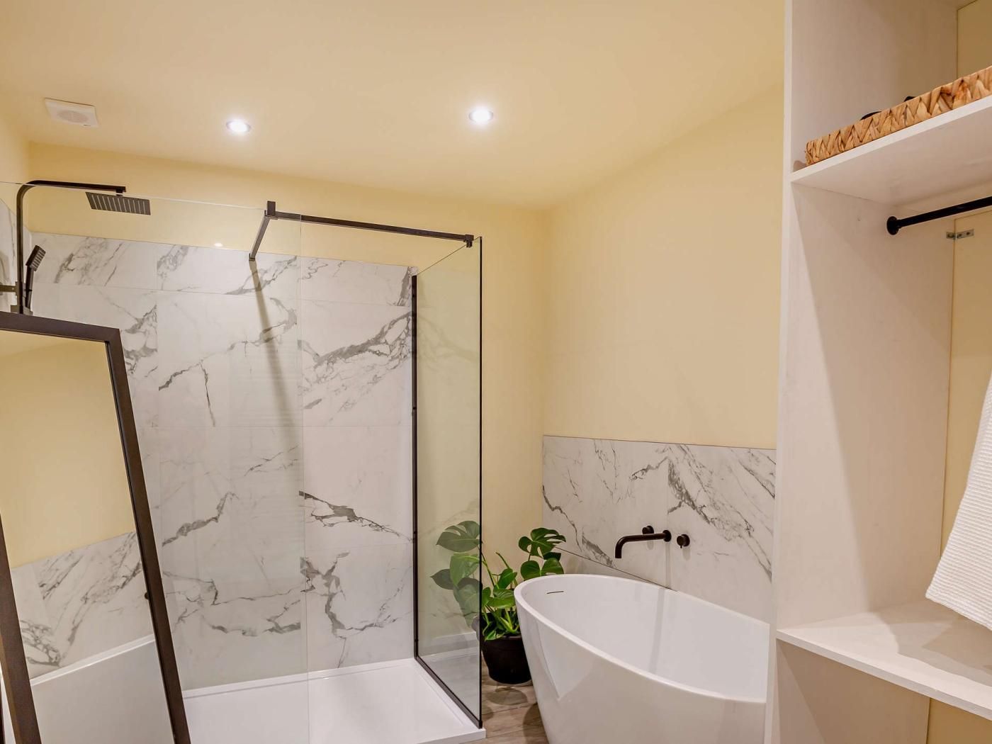 A bathroom with a glass-enclosed shower, a freestanding bathtub, and a marble-tiled wall.