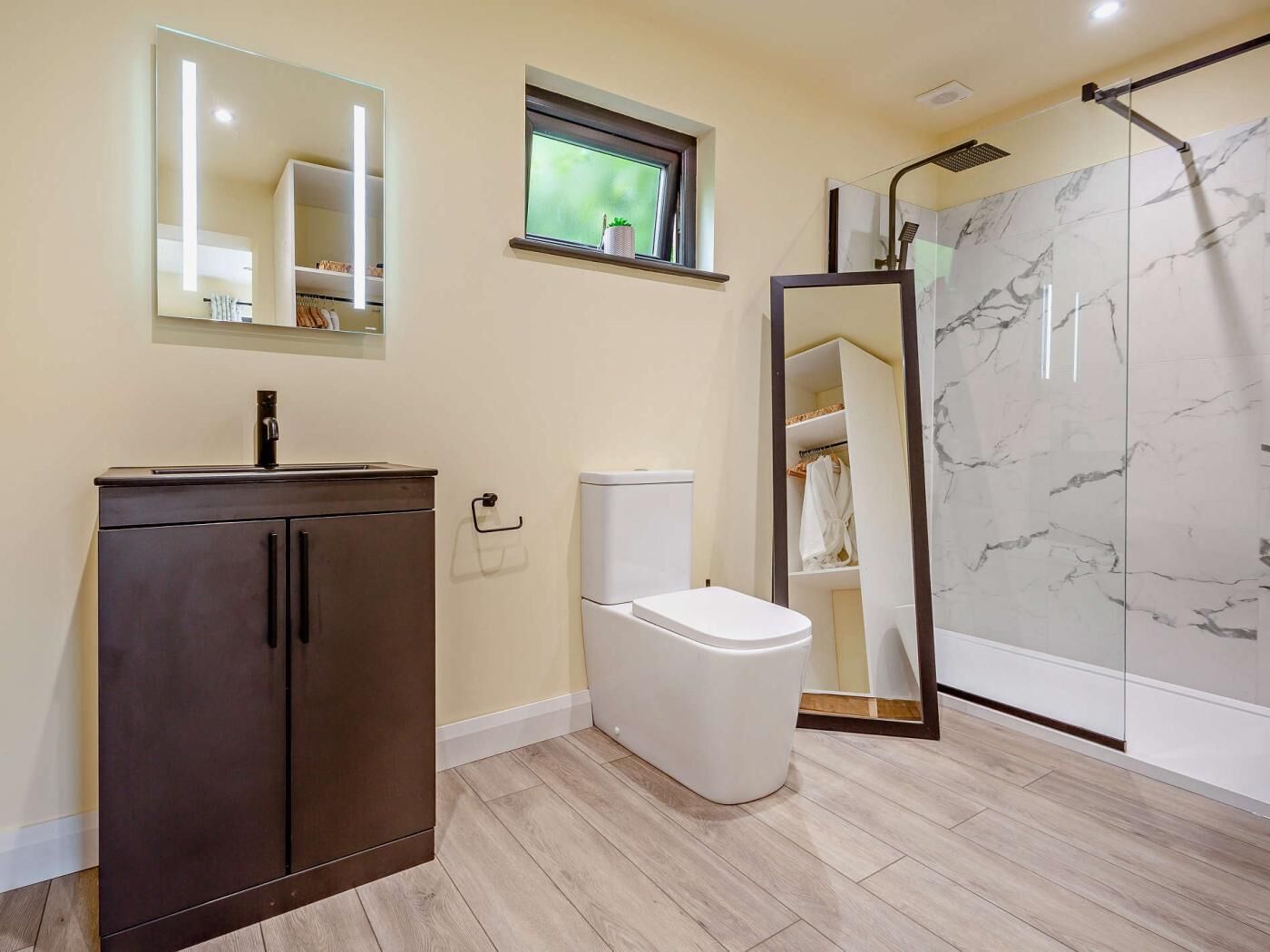 Une salle de bain avec un meuble en bois foncé, des toilettes, une cabine de douche en verre et un mur recouvert de carreaux de marbre.