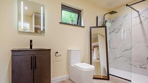 Ein Badezimmer mit einem dunklen Holzschrank, einer Toilette, einer Duschkabine aus Glas und einer Wand mit Marmorfliesen.