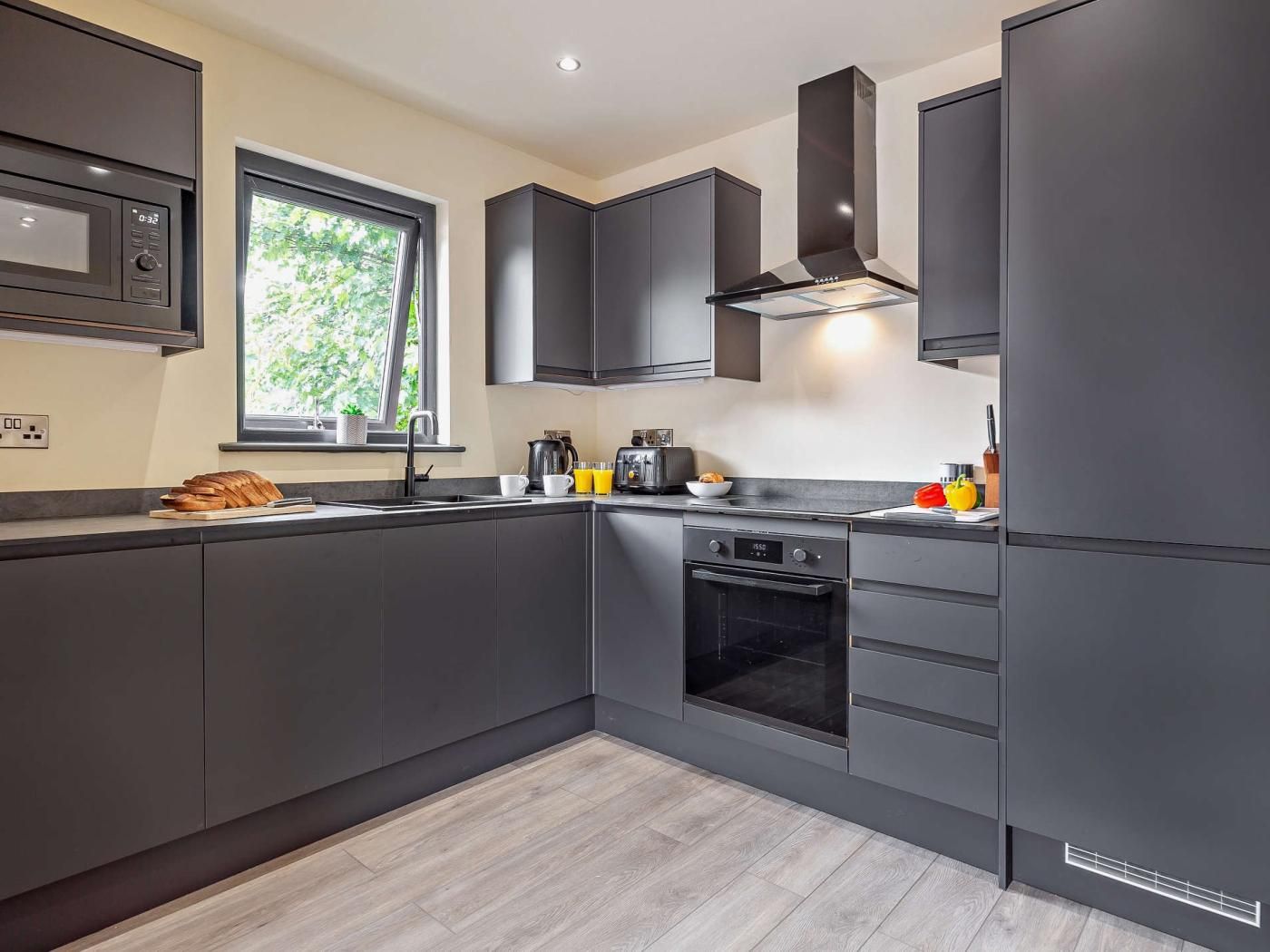A modern kitchen with dark cabinetry, a built-in oven, and a window providing natural light.
