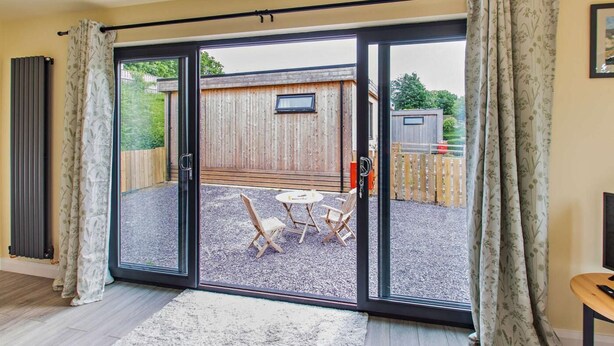 Ein Zimmer mit einer Schiebeglastür, die auf eine Außenpatioterasse mit Holzdeck, einem Tisch und zwei Stühlen führt.