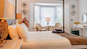 A hotel room with a large bed, a desk with a lamp, a chair, a vanity with a mirror, and a window with blinds. - 3 Bed in Shanklin (oc-92053) (Shanklin)
