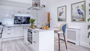 A modern kitchen with white cabinetry, a central island, and a dining area with a chair. - 3 Bed in Shanklin (oc-92053) (Shanklin)