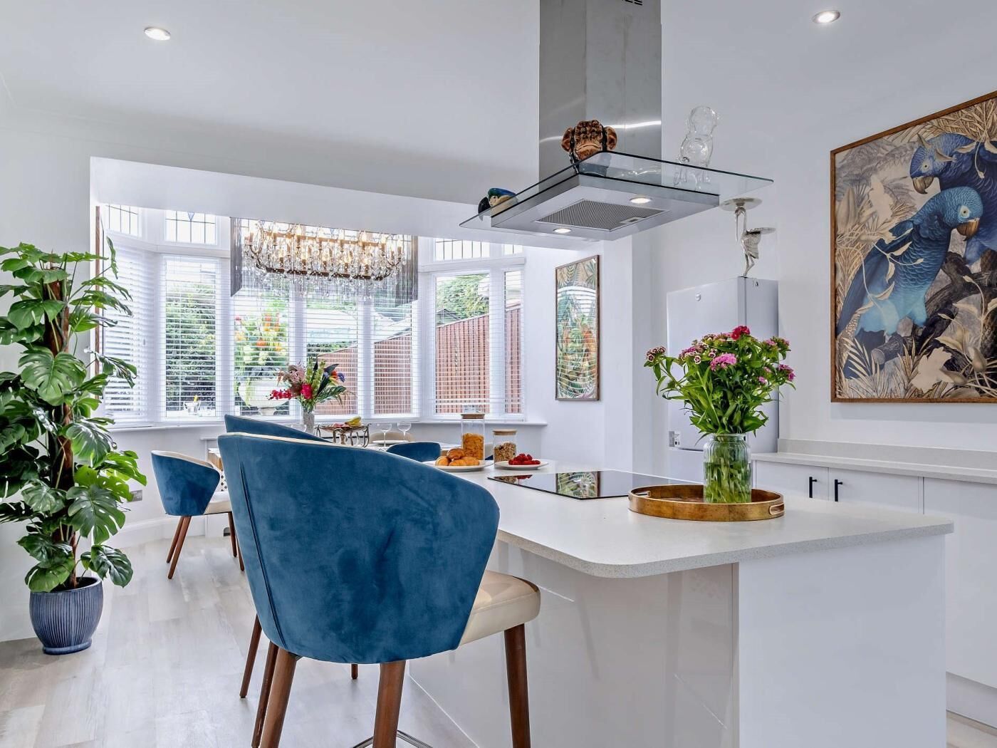 A modern kitchen with a central island, blue chairs, and a large window with a view.