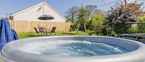 A hot tub in a backyard with a wooden fence, a table with chairs, and a house in the background.